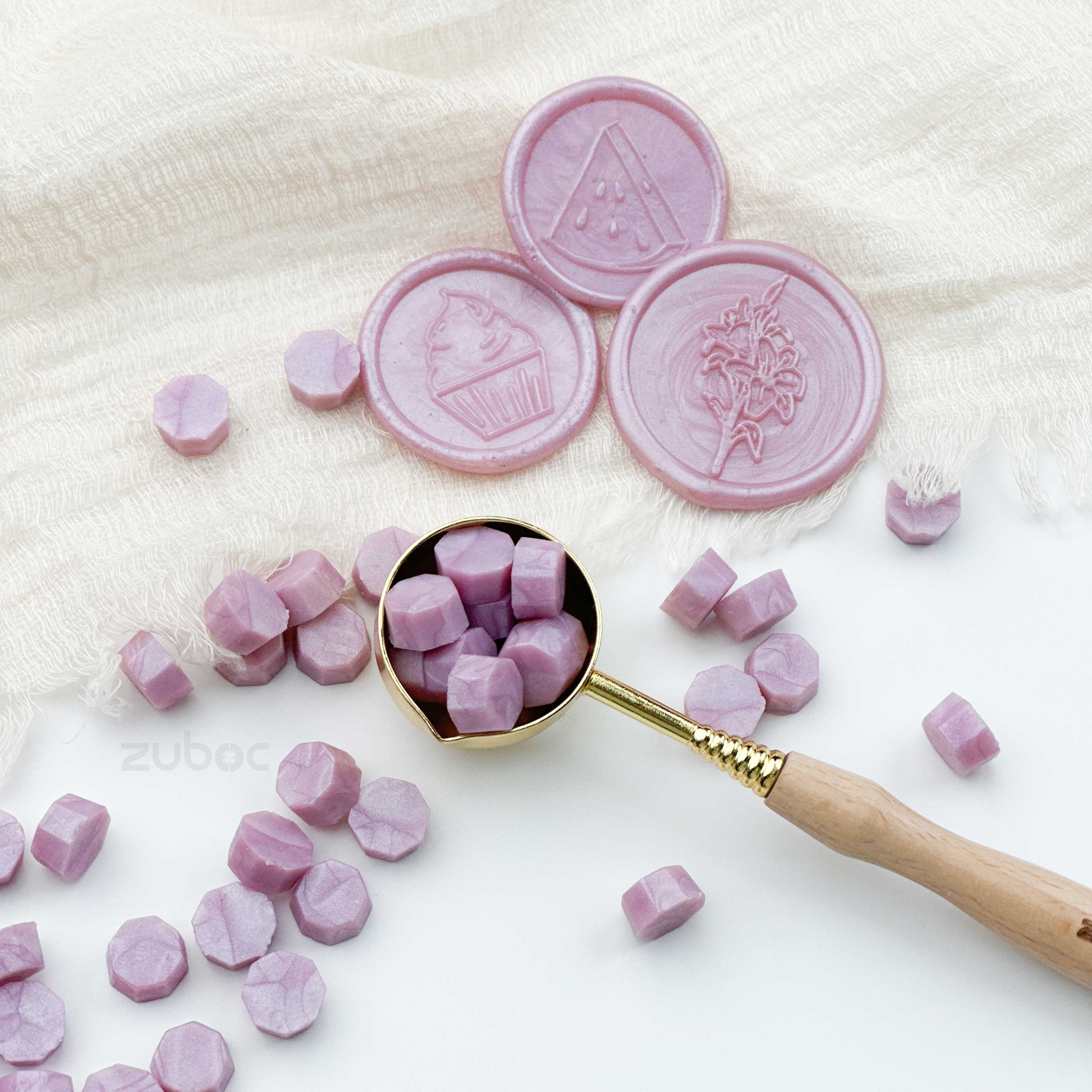 Pink candy tablets with embossed designs on a white surface, some in a gold spoon.