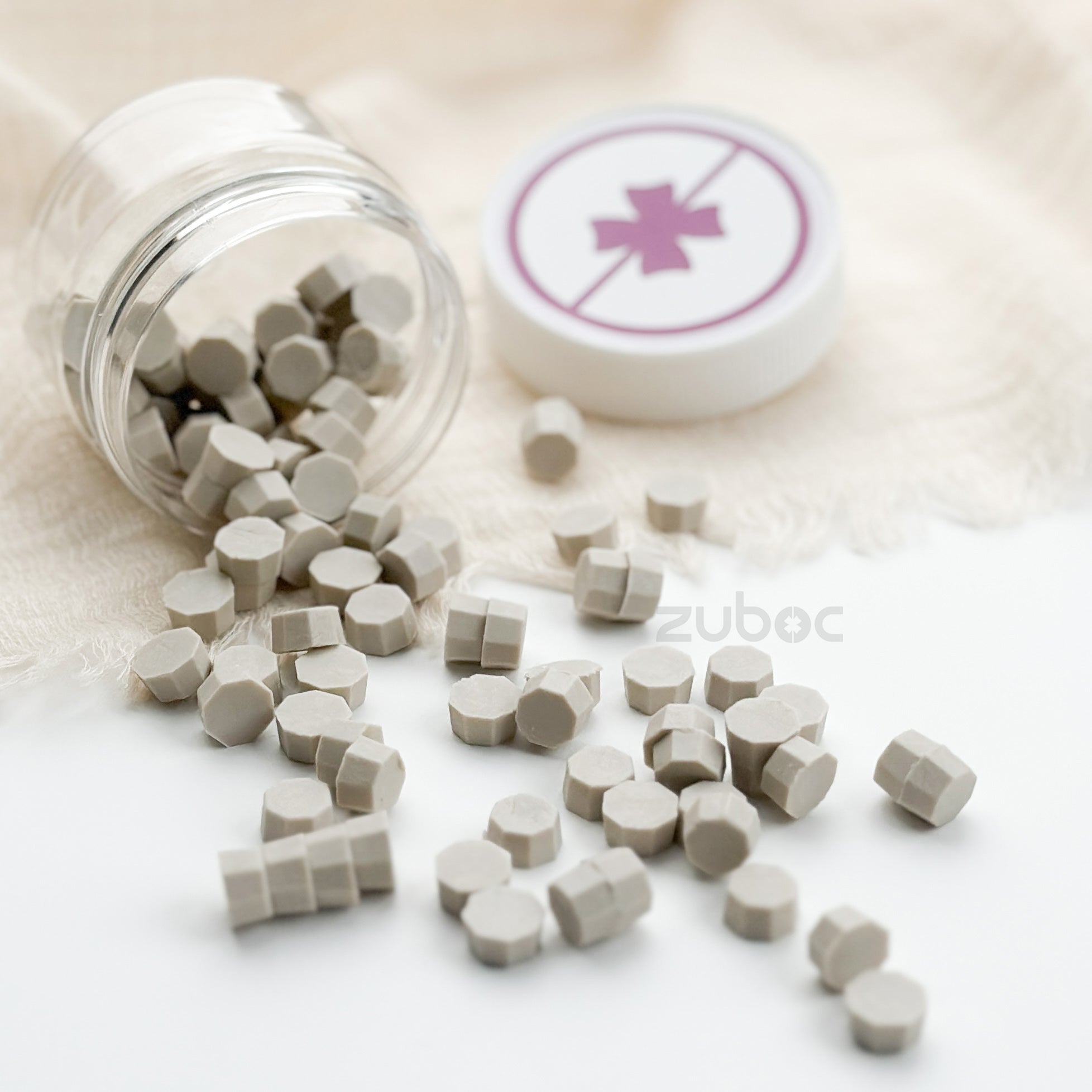 White hexagonal tablets spilling out of a transparent bottle with a white cap featuring a red cross symbol on a light beige background.