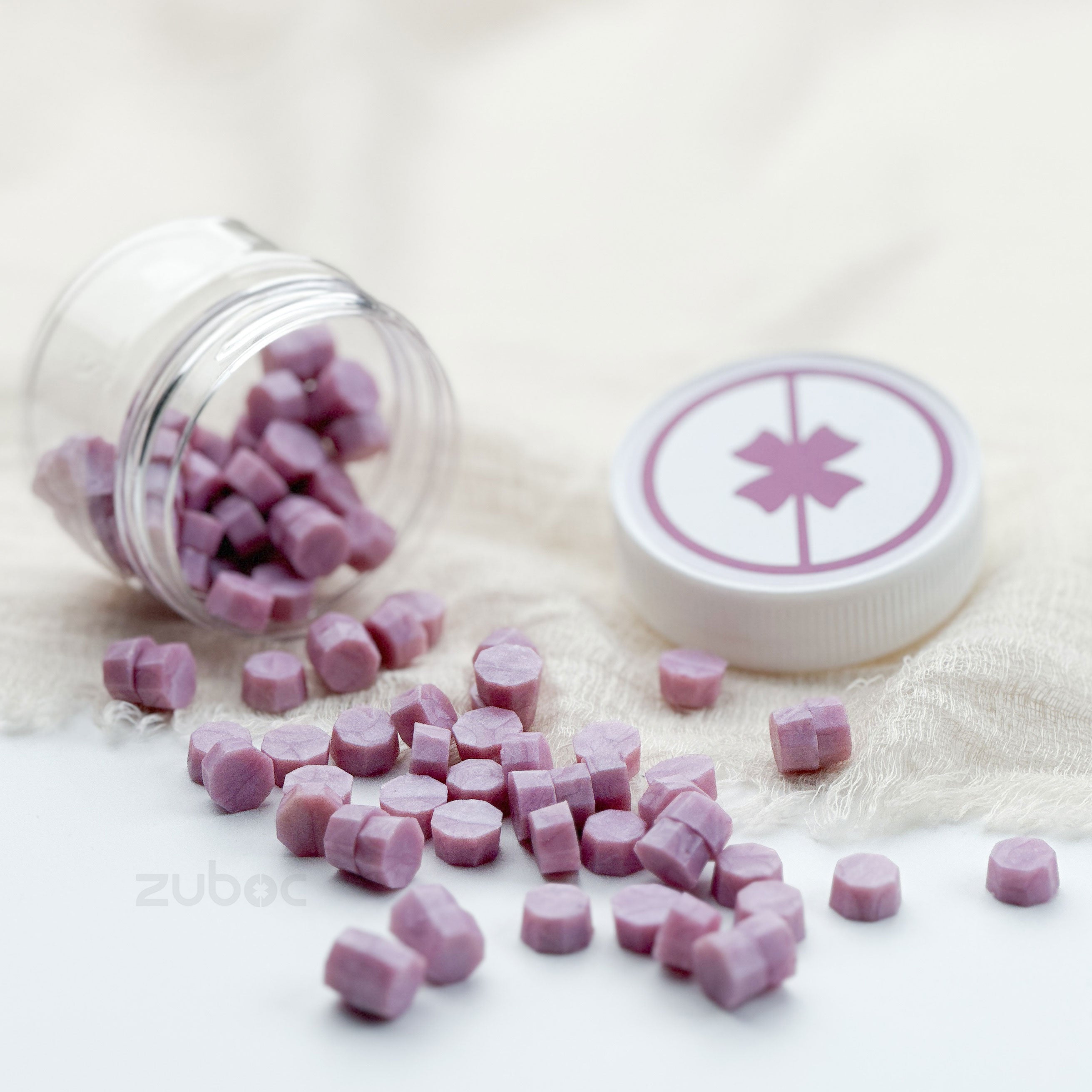 Purple candy pieces spilling out of a clear jar with a white lid featuring a pink star symbol on a light background.